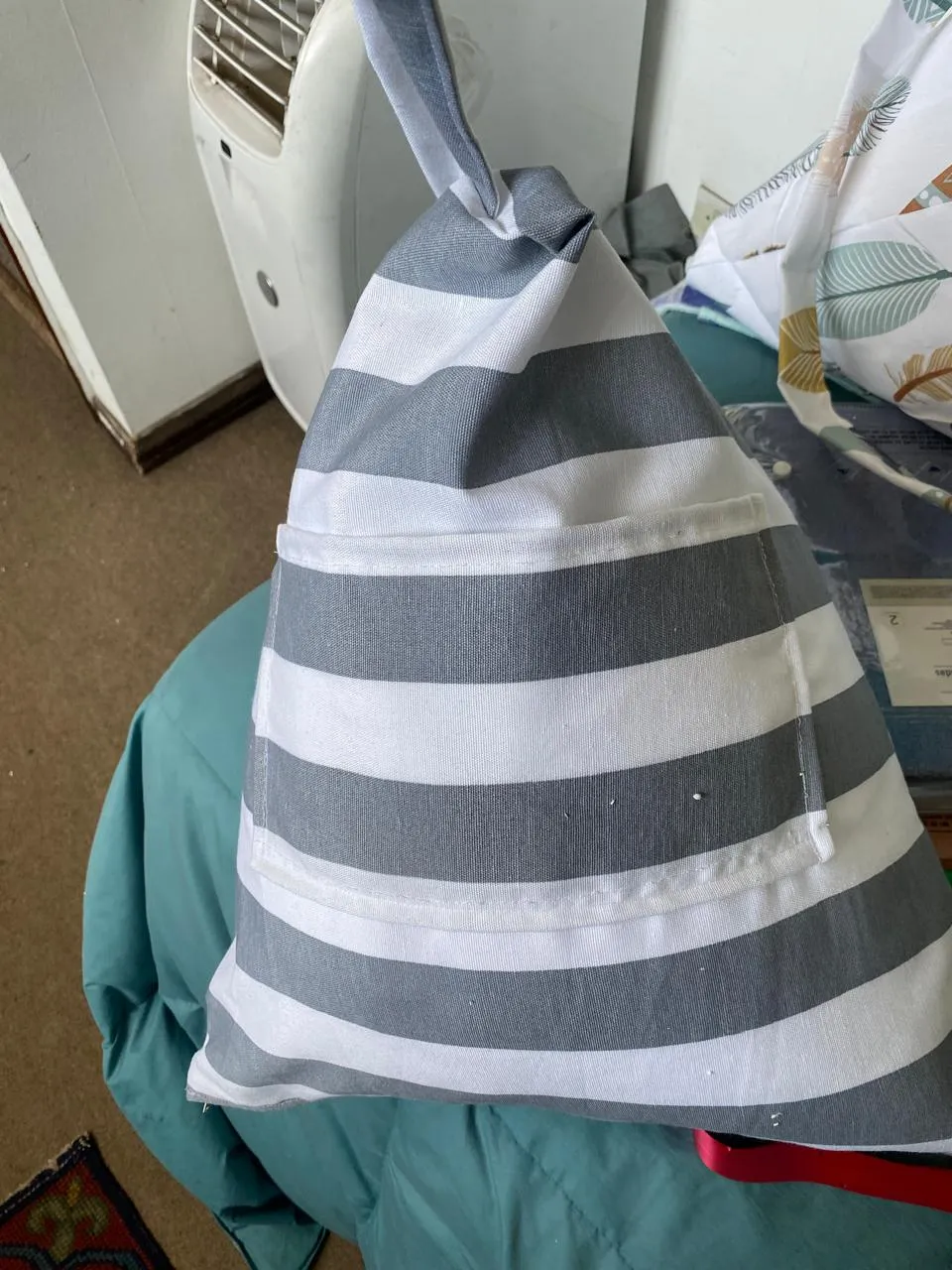 Cojín con tela de rayas grises y blancas, con bolsillo y asa